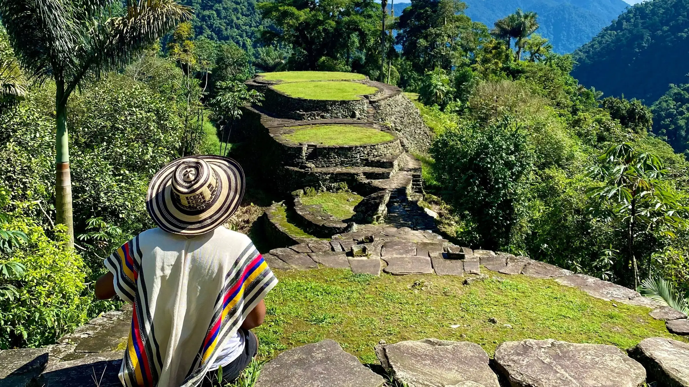 A hiker in a sombrero vueltiao looks out over the stone terraces of Colombia's Lost City in the forest