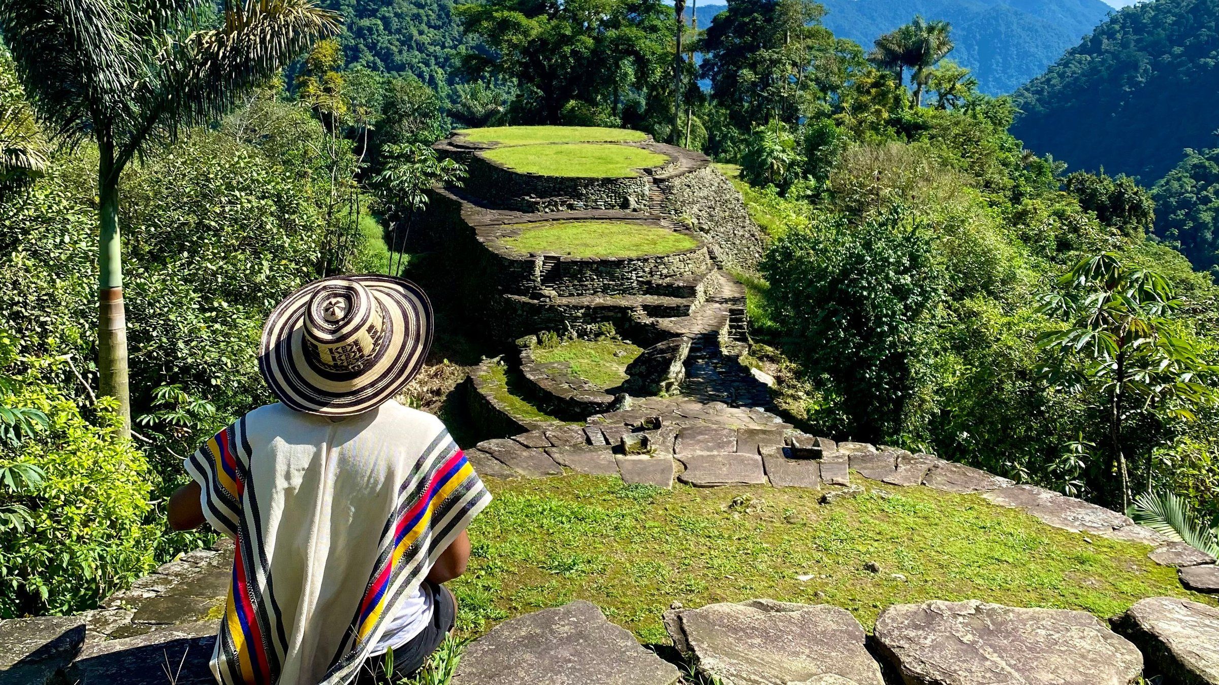 Un caminante con sombrero vueltiao mira las terrazas de piedra de Ciudad Perdida en medio de la selva