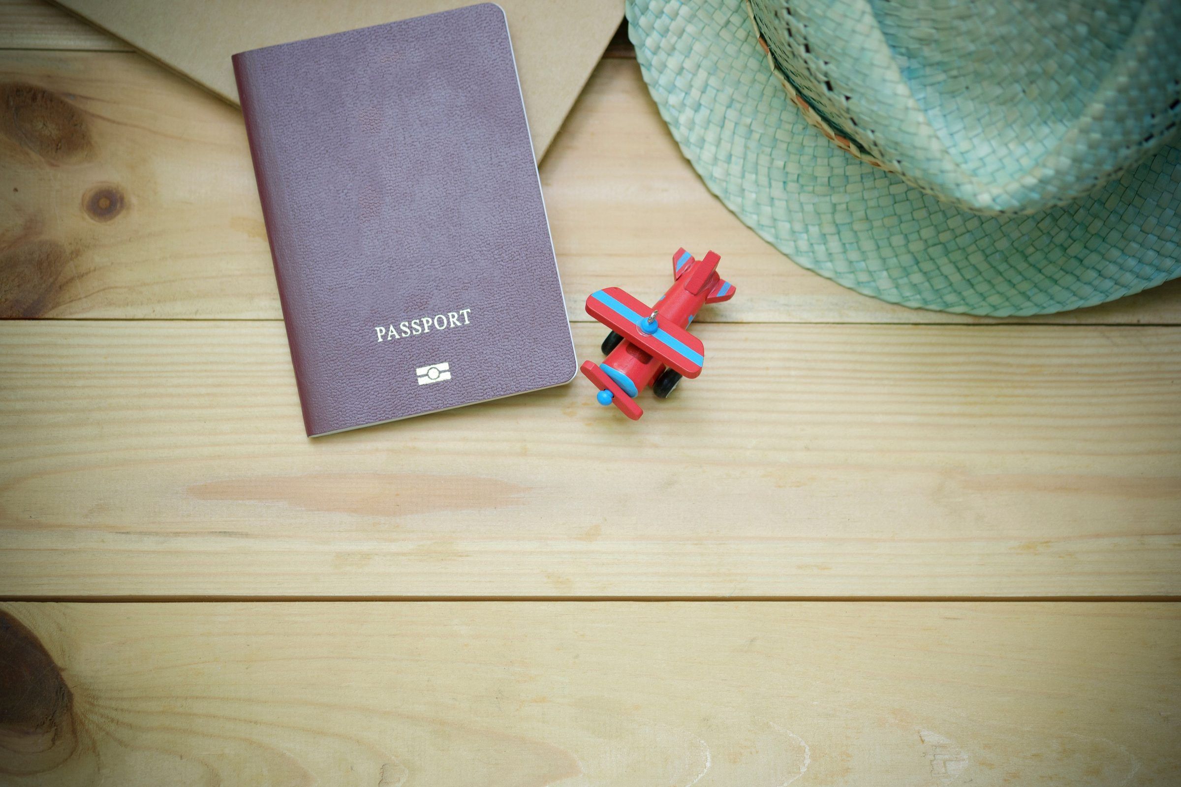 A passport, a straw hat and a toy plane on a wooden table