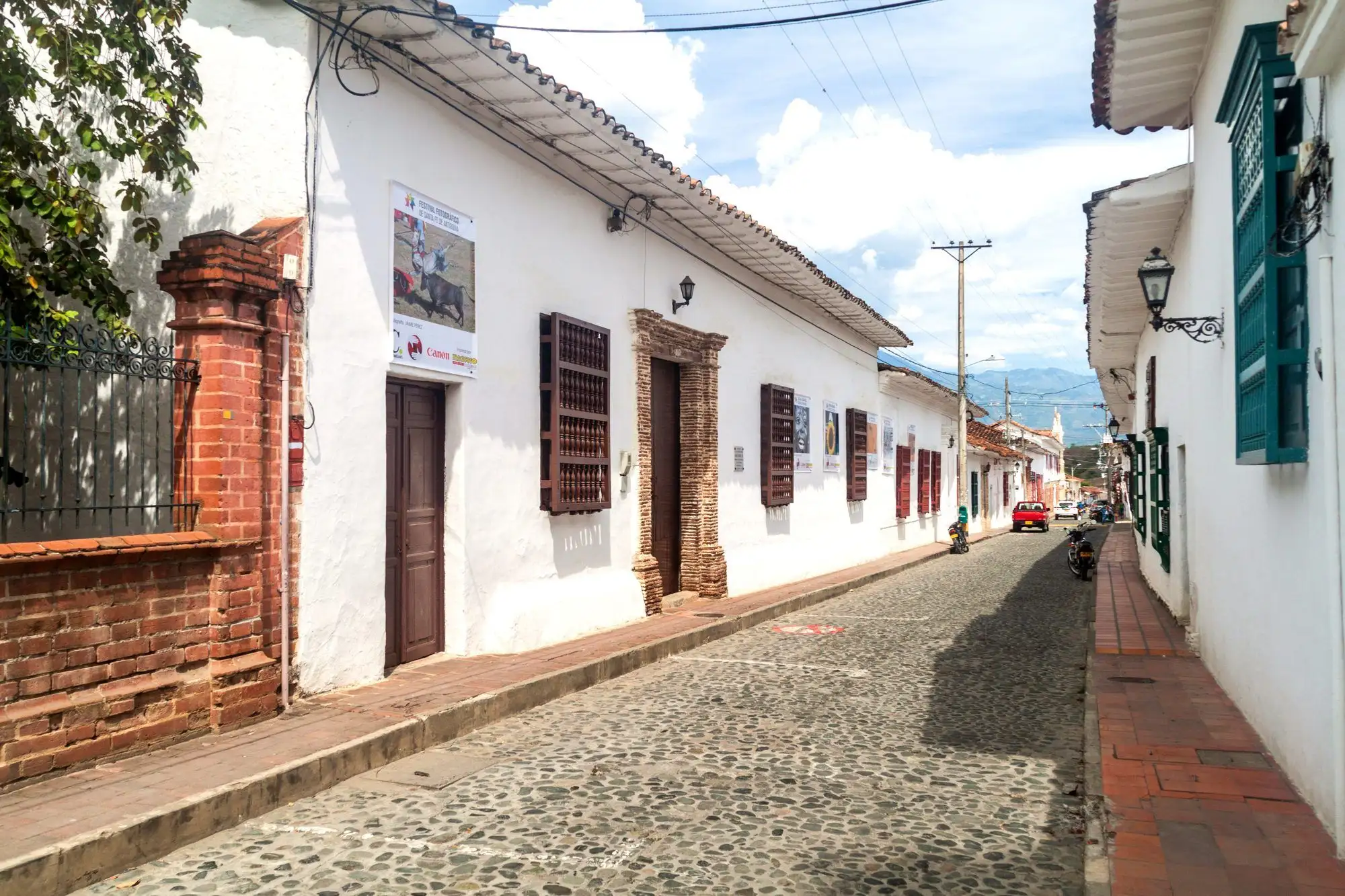 Una calle empedrada del centro histórico de Santa Fe de Antioquia con casas blancas, ventanas de madera con rejas y las montañas al fondo