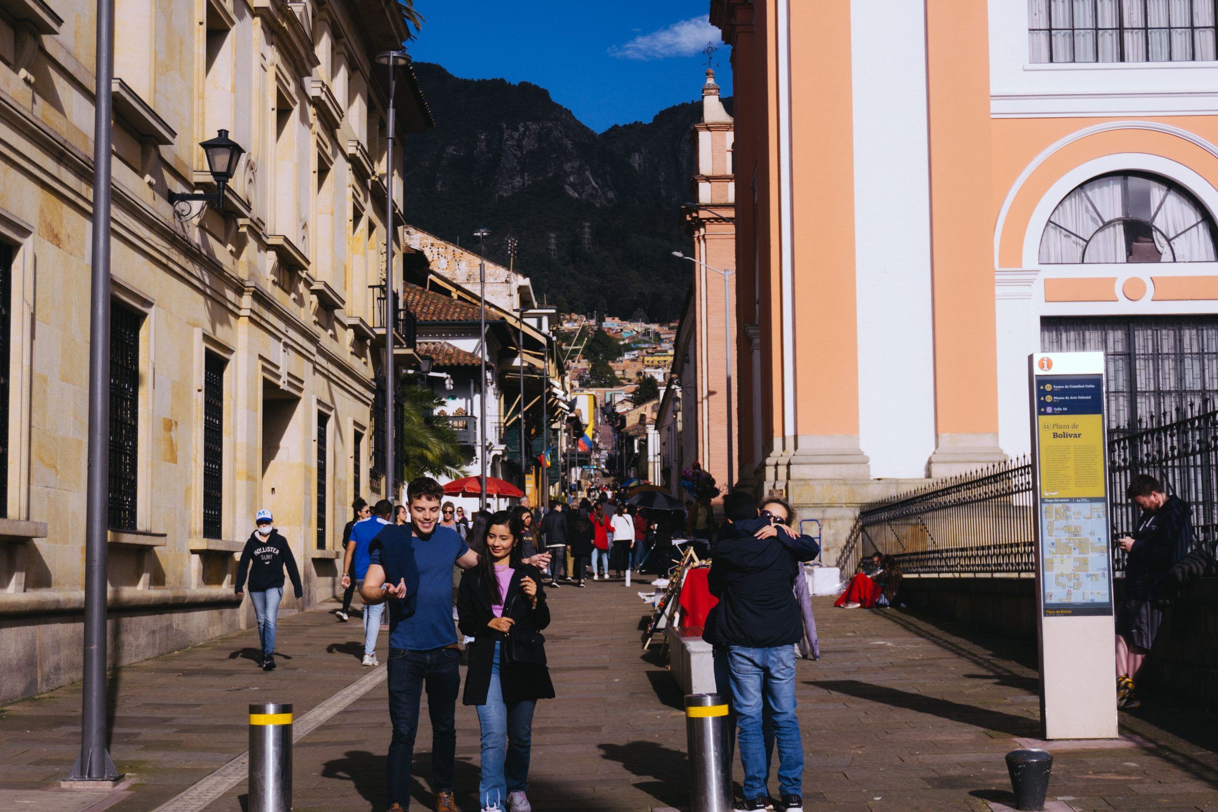 People walking down a street in a historic centre, between colonial buildings with mountains behind